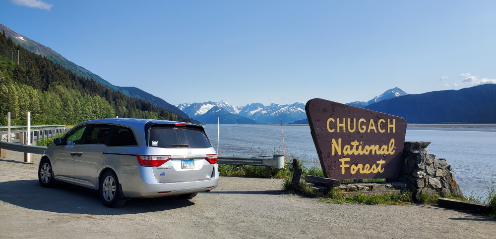 Minivan next to a national forest sign with mountains in the background